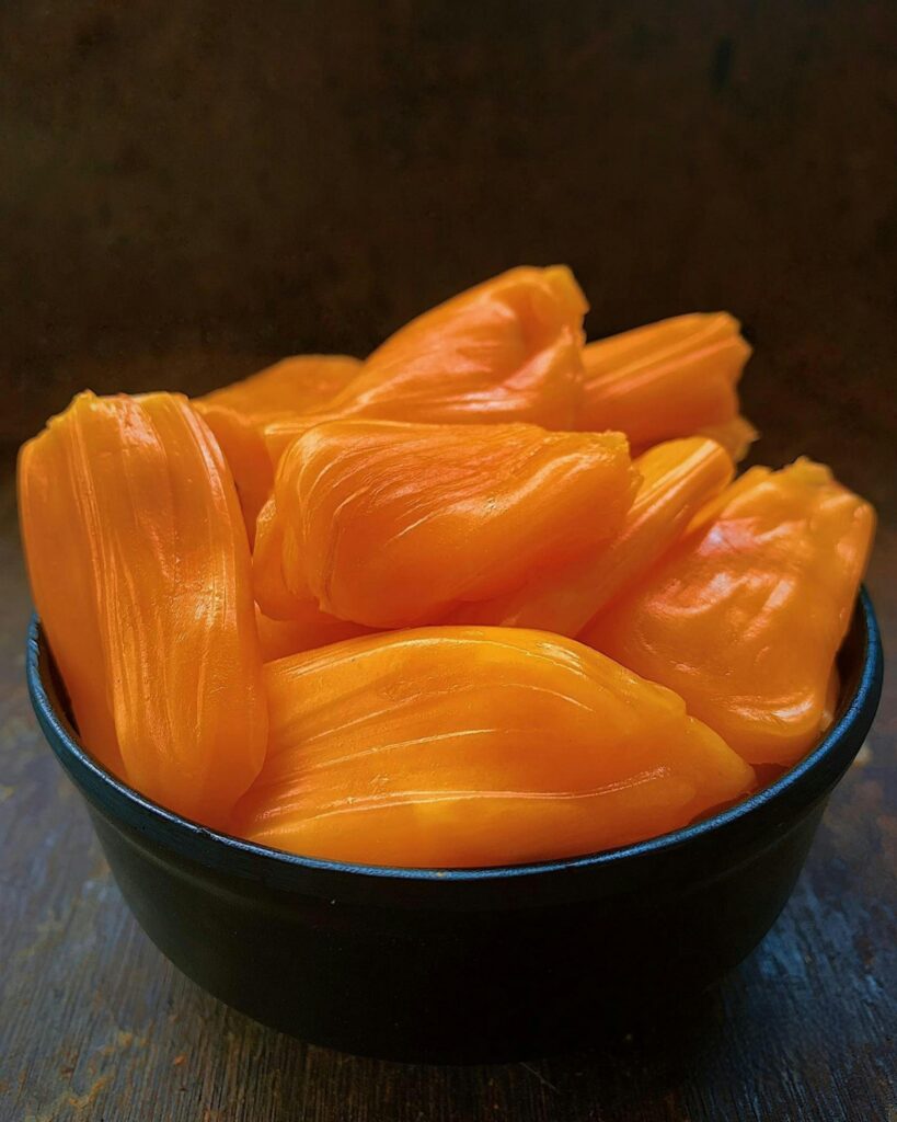 Vibrant orange jackfruit flesh in a dark bowl, showcasing freshness and exotic appeal.